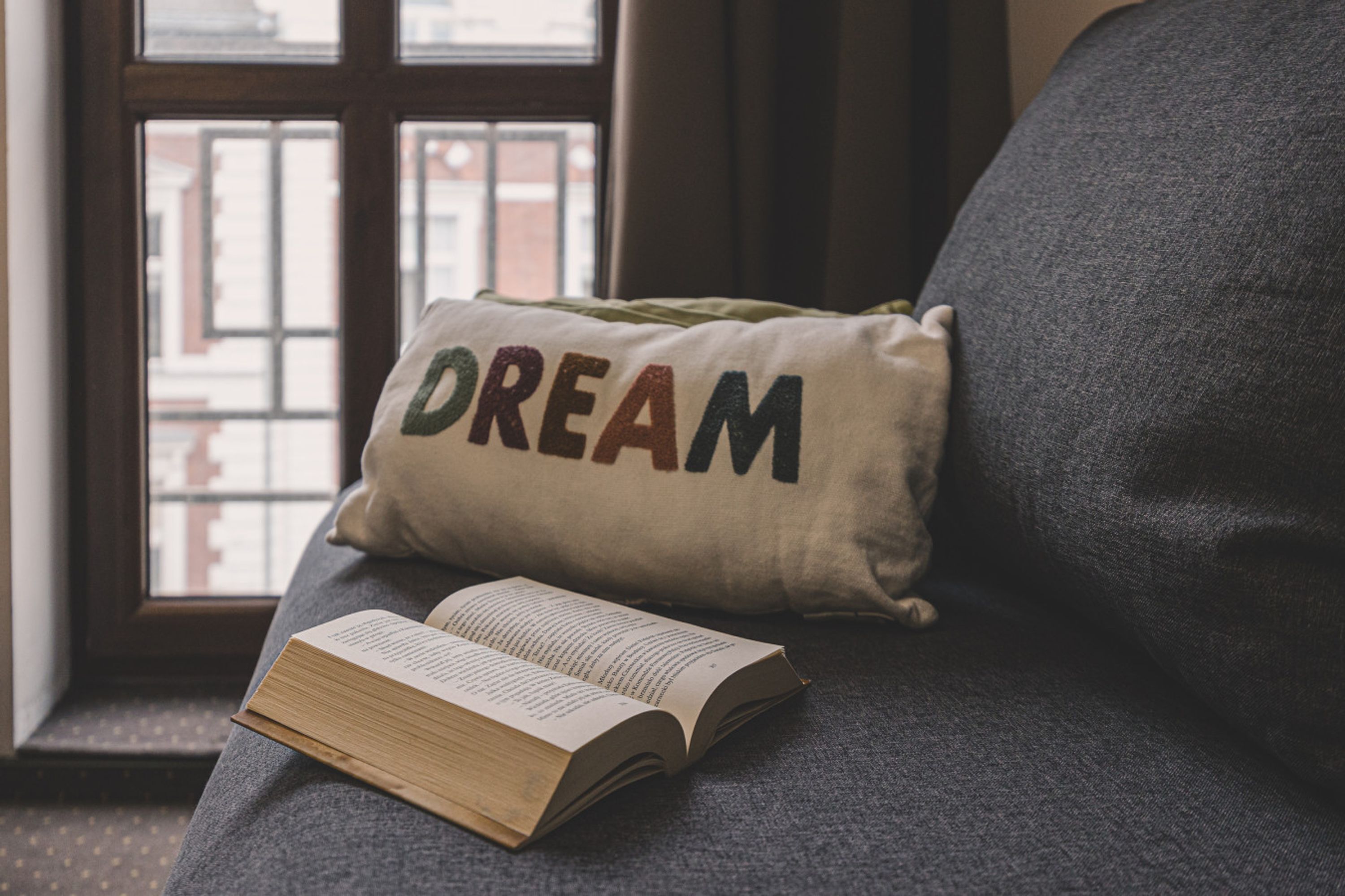 A book on a couch with a pillow that has the word "DREAM" on it.