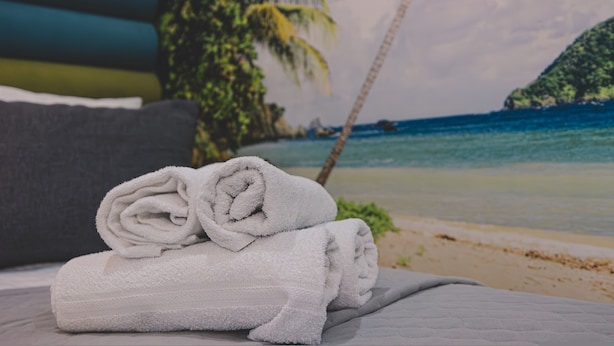 A neatly folded white towel on a bed with a view of a beach and palm trees. - Dream 23A Studio z Przeszklon Azienk Centrum (Bydgoszcz)