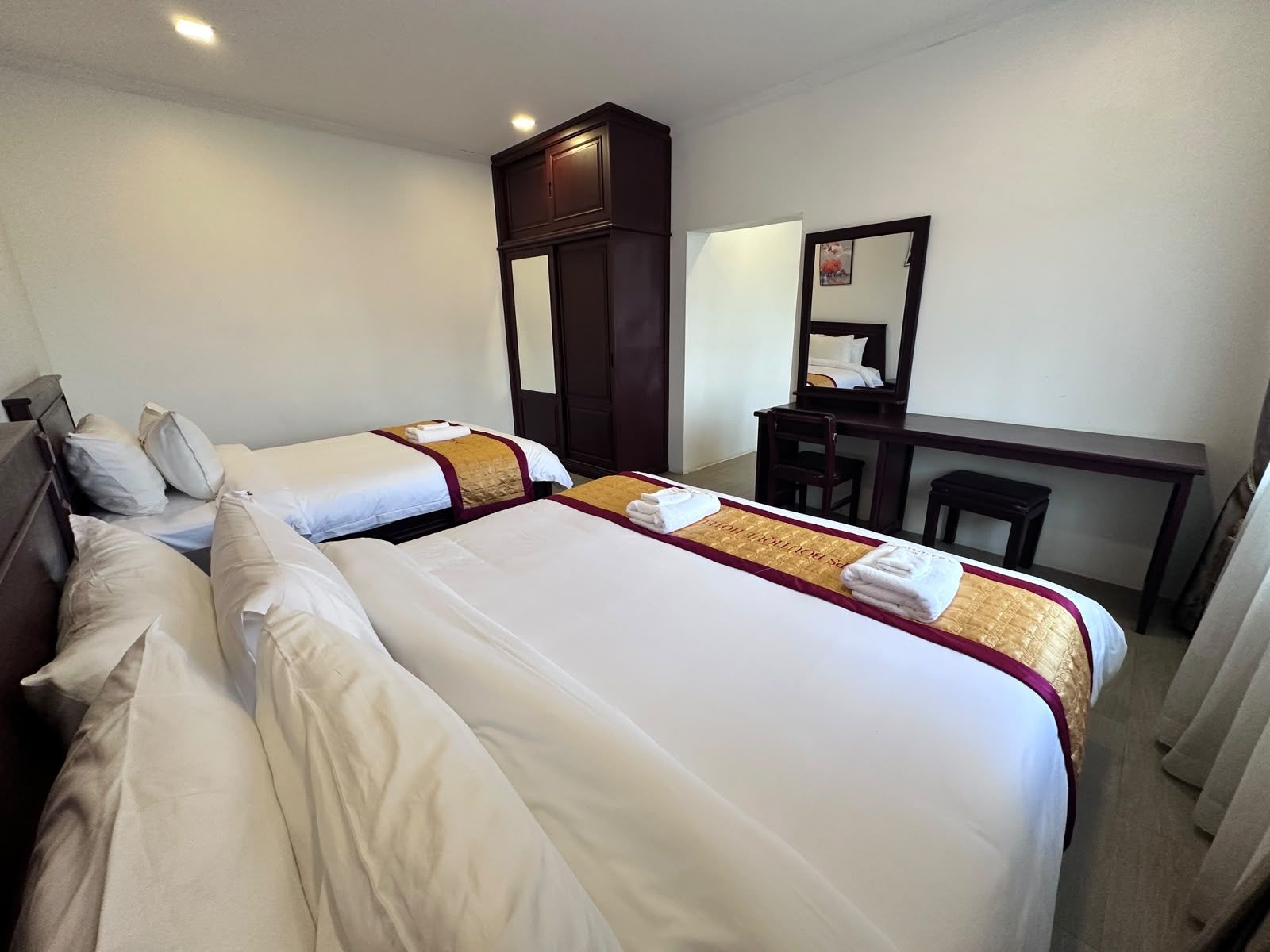 Quarto de hotel com duas camas, uma escrivaninha, uma cadeira e um guarda-roupa.