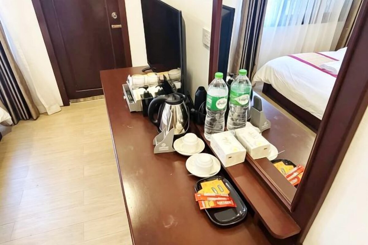 A hotel room with a wooden desk, a bed, a television, and a window with curtains.