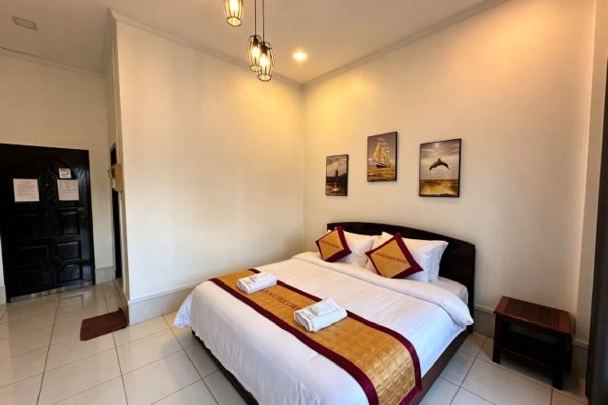 Habitación de hotel con una cama grande, una mesita de noche, una puerta y una pared con tres cuadros.