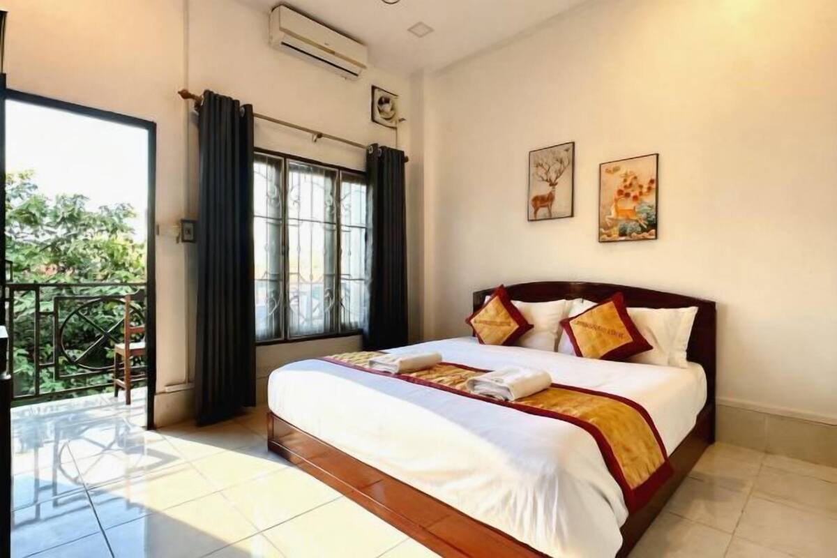 A hotel room with a bed, a window with curtains, a balcony, and artwork on the wall.