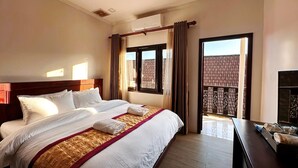A hotel room with a large bed, a wooden headboard, a bedside table with a mirror, and a view of a building through the window. - Vang Vieng Family Boutique Hotel (Vang Vieng)