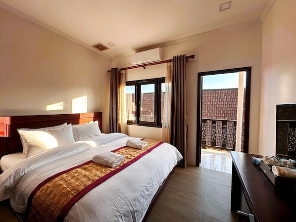 Una camera d'albergo con un letto grande, una testiera in legno, un comodino con uno specchio e vista su un edificio dalla finestra.