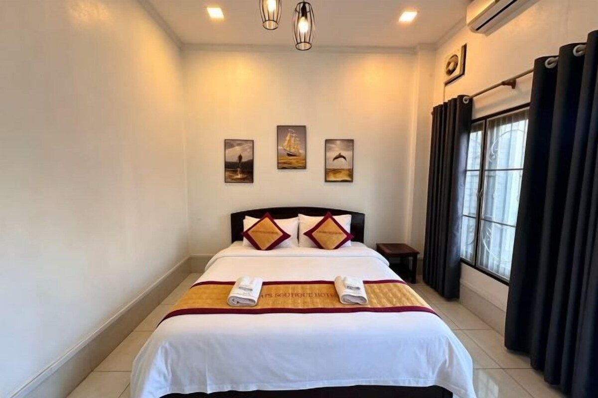 A hotel room with a bed, a nightstand, a window with curtains, and wall art.