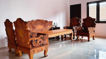 A room with ornate wooden furniture, including a sofa and chairs, with a tiled floor and a window with blinds.