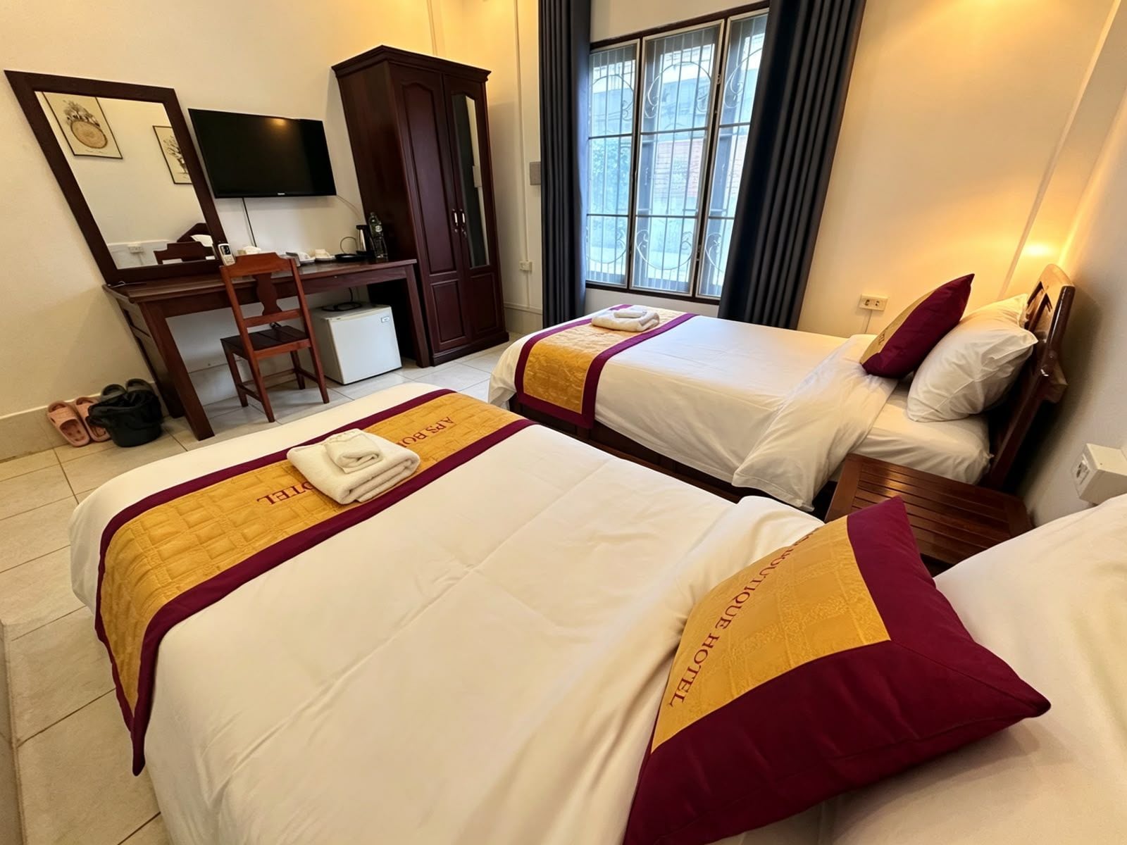 A hotel room with two beds, a desk, a chair, a TV, and a wardrobe.