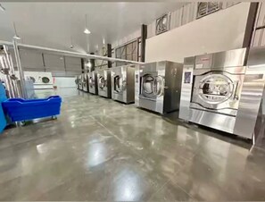 Un lavadero industrial con varias lavadoras de acero inoxidable alineadas sobre un piso de concreto pulido.