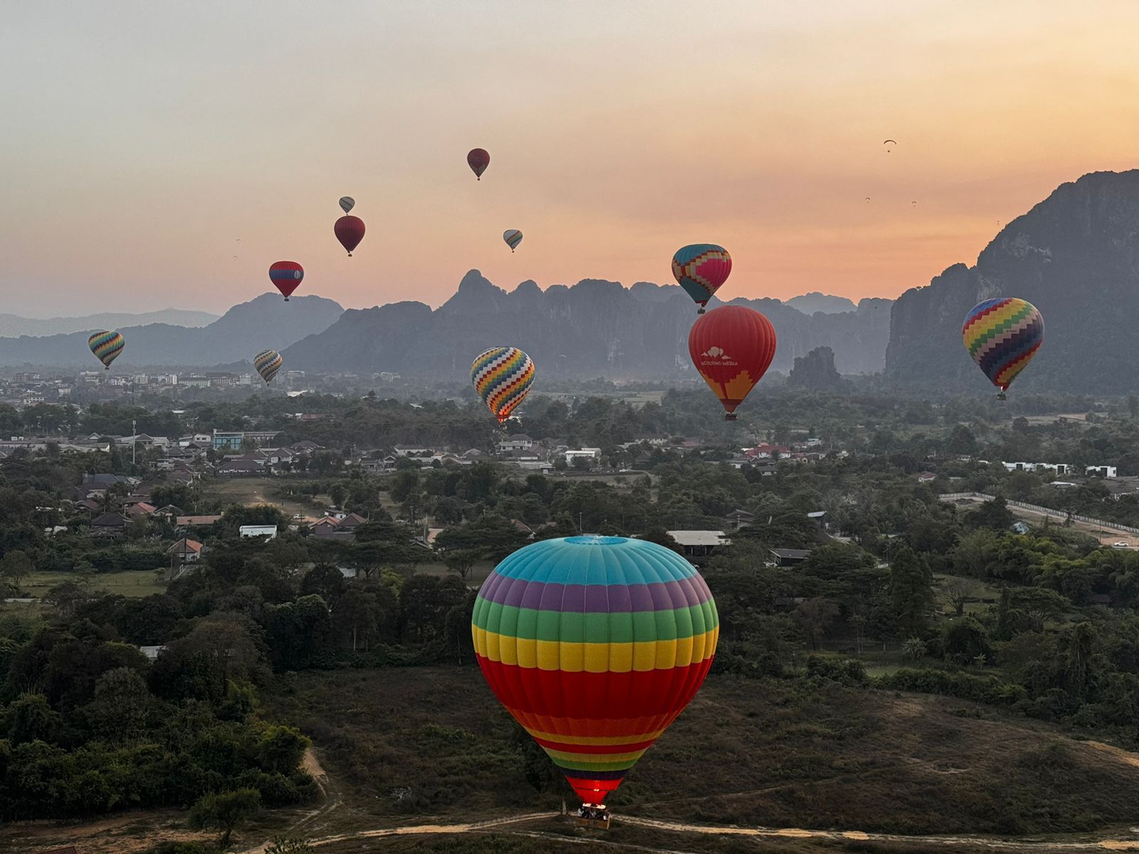 A landscape with multiple hot air balloons, a mountainous backdrop, and a town below.