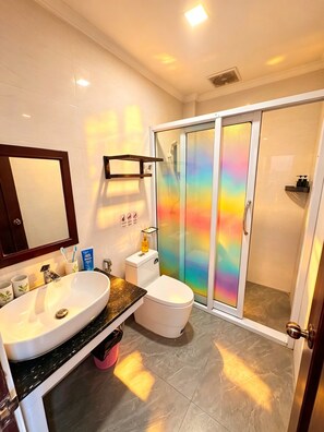 A bathroom with a large mirror, a sink, a toilet, and a shower with a glass door. - Vang Vieng Family Boutique Hotel (Vang Vieng)