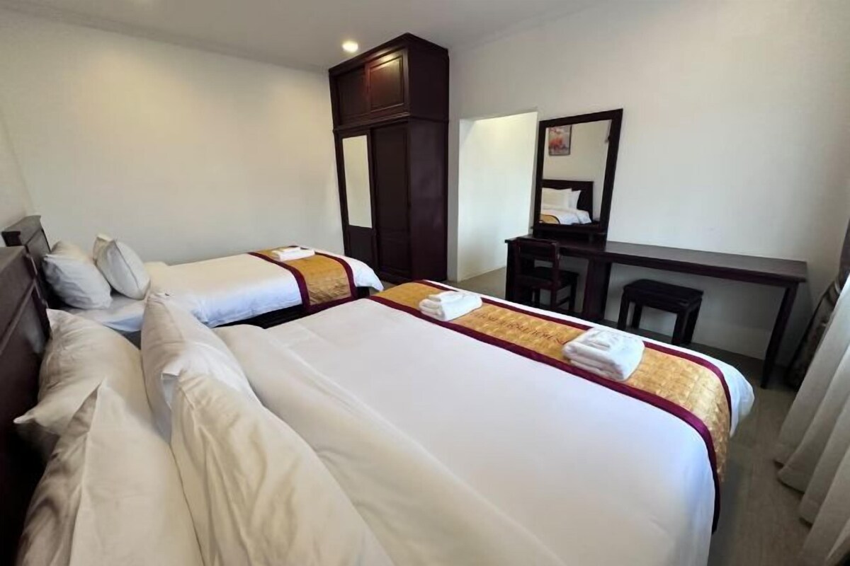 A hotel room with two beds, a desk, a chair, and a wardrobe.