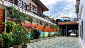 A courtyard with a tiled floor, potted plants, and a building with a balcony. - Vang Vieng Family Boutique Hotel (Vang Vieng)
