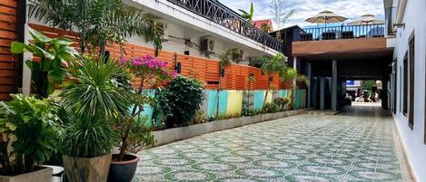 A courtyard with a tiled floor, potted plants, and a building with a balcony.