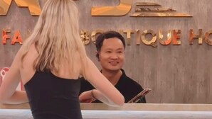 A woman standing at a reception desk in a hotel lobby with a sign that reads "ABS" and "HOTEL". - Vang Vieng Family Boutique Hotel (Vang Vieng)