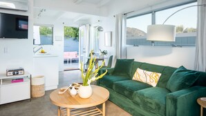 Ein modernes Wohnzimmer mit einem grünen Sofa, einem runden Holztisch und einem an der Wand befestigten Fernseher.