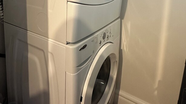 A stacked washer and dryer unit in a room with a plain wall and wooden flooring. - Beautiful place with Kitchen, Washing Machine, Internet near UBC, beach and DT (Vancouver)