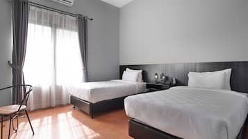 A hotel room with two beds, a chair, a bedside table with a lamp, and an air conditioning unit.