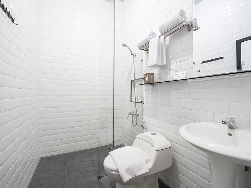 A modern bathroom with white subway tiles, a glass shower enclosure, a white toilet, and a white sink.