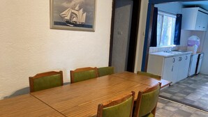 Een eethoek met een houten tafel en groene fauteuils. Daarboven hangt een schilderij op de muur. Achtergrond is een keuken met witte kasten en een raam.