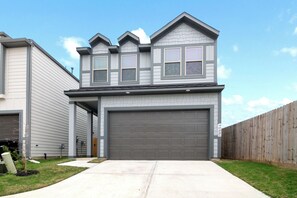 Une maison à deux étages avec un garage, une cour arrière clôturée et un ciel dégagé.