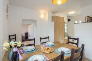 A dining area with a wooden table set for four, surrounded by chairs. There is a vase with flowers on the table, and a bottle of wine is visible.