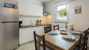 Una cocina moderna con armarios blancos, un refrigerador de acero inoxidable y una mesa de comedor para cuatro.