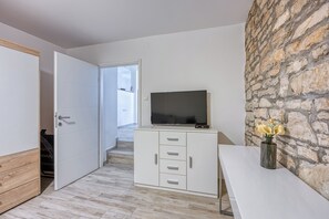 Ein modernes Zimmer mit einer Steinwand, einem Flachbildfernseher auf einer Kommode, einem weißen Schreibtisch und einer Holztür.
