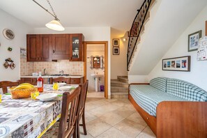 Una cucina con mobili in legno, un tavolo da pranzo con sedie, una scala e un letto con copriletto a quadri.