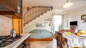 A kitchen with a gas stove, wooden cabinets, a checkered sofa, a dining table with chairs, and a staircase. - Casa Machiavelli Near The Sea, Porto Cesareo, Italy (Porto Cesareo)