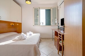 A hotel room with a bed, a desk, a television, and a window with open shutters.