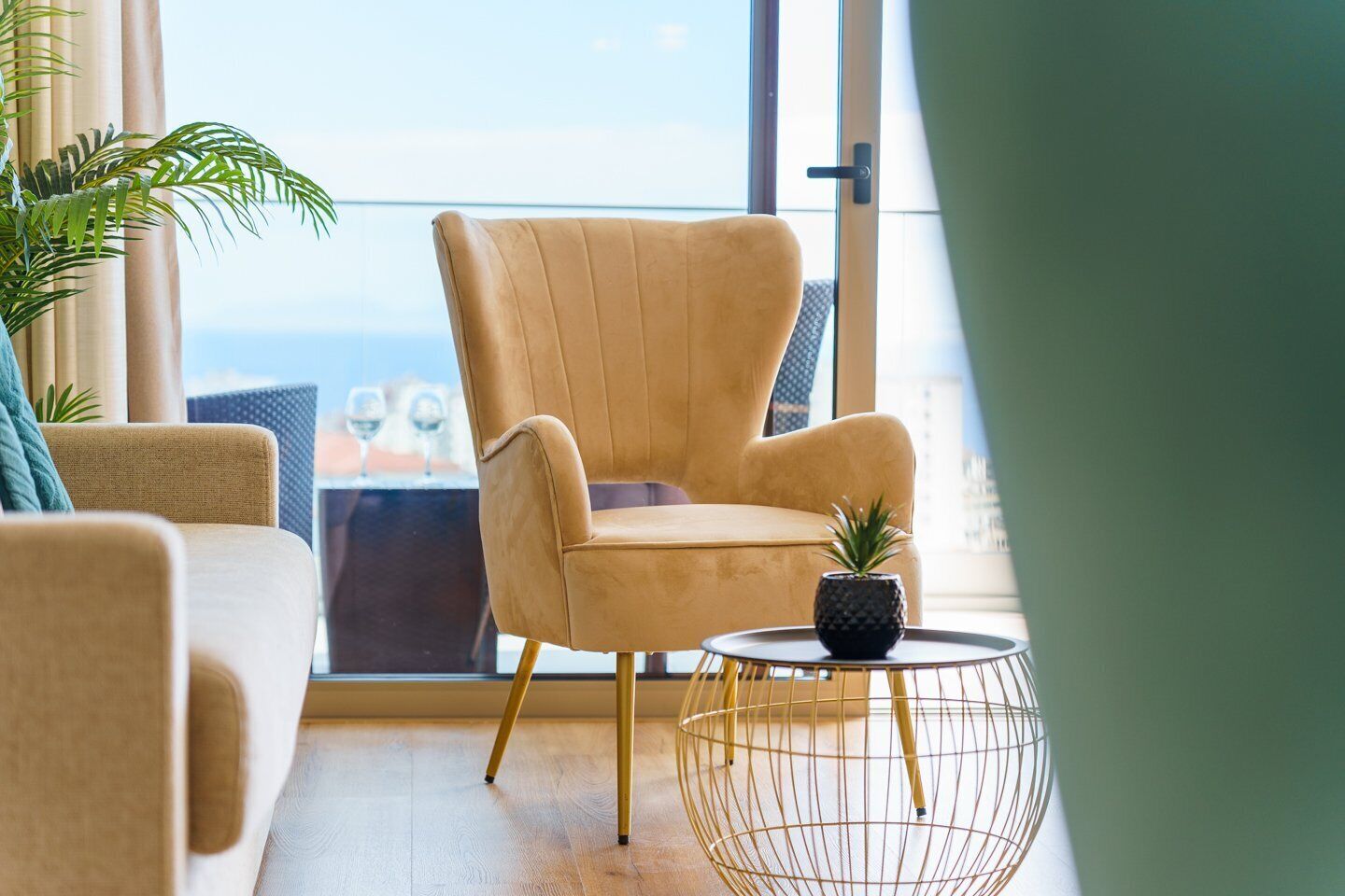 A modern living room with a beige armchair, a round coffee table with a potted plant, and a view of the city through large windows.