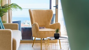 A modern living room with a beige armchair, a round coffee table with a potted plant, and a view of the city through large windows. - GuestReady - The perfect place to relax in Funchal (Funchal)