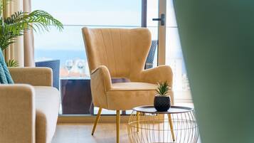 A modern living room with a beige armchair, a round coffee table with a potted plant, and a view of the city through large windows.