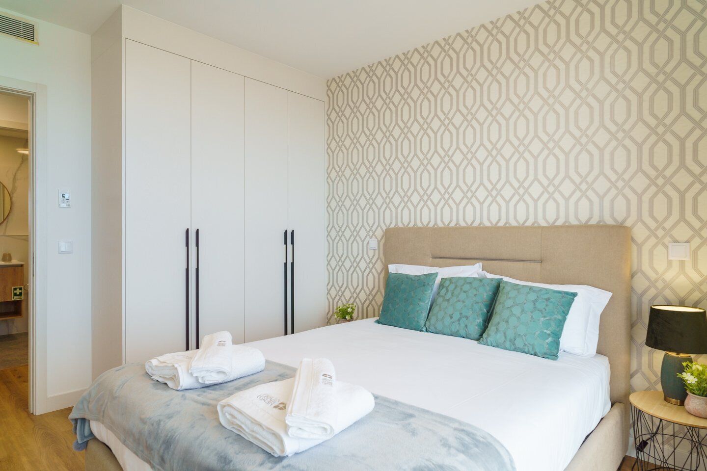 Una habitación de hotel con una cama, dos mesitas de noche, un armario y una pared con diseño.