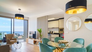 A modern living room with a glass table, teal chairs, and a flat-screen TV. - GuestReady - The perfect place to relax in Funchal (Funchal)