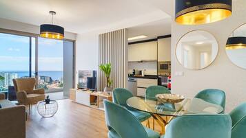 A modern living room with a glass table, teal chairs, and a flat-screen TV.