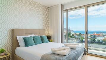A modern hotel room with a large bed, a view of the city, and a patterned wall.
