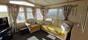 A cozy living area with a sofa, armchairs, a television, and curtains.