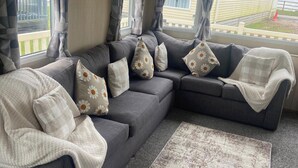 A living room with a grey sofa, multiple pillows, a white throw blanket, and a patterned rug. - Seaside Retreat-Sleeps 8-Free Parking (Morecambe)