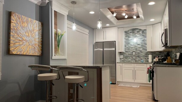 A modern kitchen with a central island, bar stools, a stainless steel refrigerator, and a backsplash with mosaic tiles. - Charming 3-bedroom house in Park Forest with WiFi, Large Flat Panel TVs & Google (Park Forest)