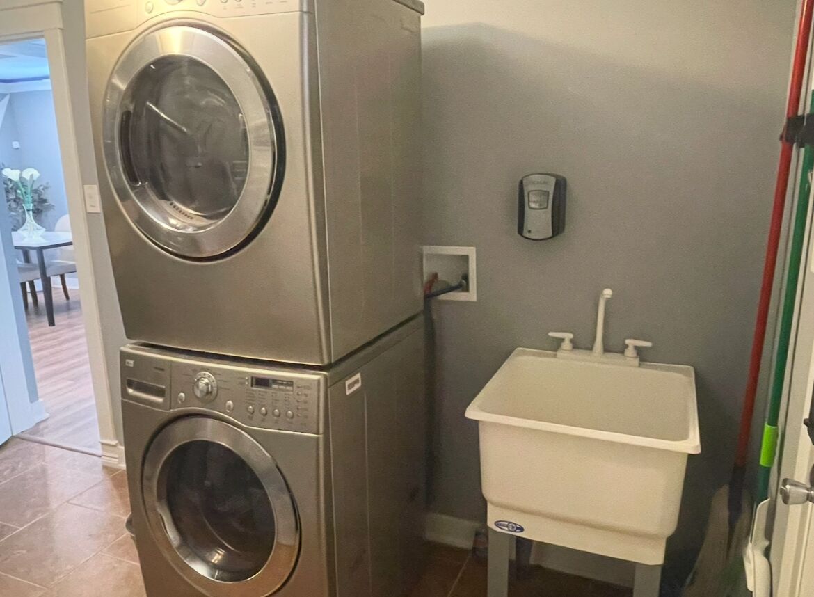 A compact laundry area with a stacked washer and dryer, a small sink, and a wall-mounted telephone.