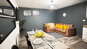 Een moderne woonkamer met een hoekbank, een eettafel gedekt voor vier personen, en decoratieve muurkunst.