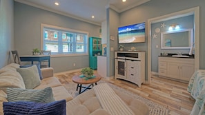 A living room with a sofa, a coffee table, and a TV. There is a kitchen area with cabinets and a refrigerator. - 2 Units Beach Boardwalk, Pool, Pickleball + Tennis Island Retreat Complex (Port Aransas)
