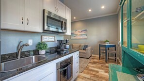 A compact kitchen with a stainless steel sink, a built-in microwave, and a coffee maker. There is a beige sofa and a small table with chairs in the adjacent living area. - 2 Units Beach Boardwalk, Pool, Pickleball + Tennis Island Retreat Complex (Port Aransas)