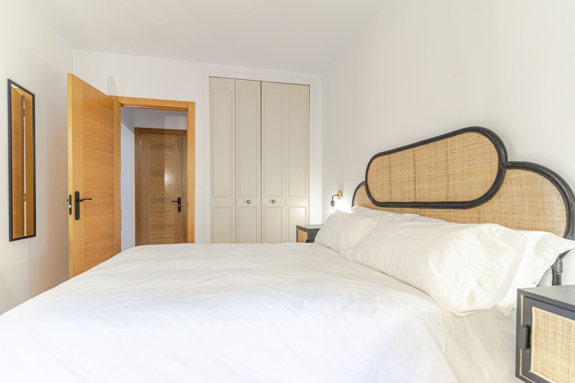 Een slaapkamer met een bed, houten deuren, een garderobe en een nachtkastje.