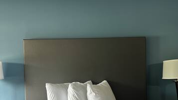 A neatly made bed with a quilted white duvet and two pillows, a dark headboard, and a bedside table with a lamp.