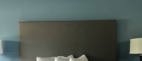 A neatly made bed with a quilted white duvet and two pillows, a dark headboard, and a bedside table with a lamp.