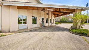 A building with a covered parking area, a single entrance, and a small garden with a tree. - LakeWood Inn & Suites (Dowagiac)