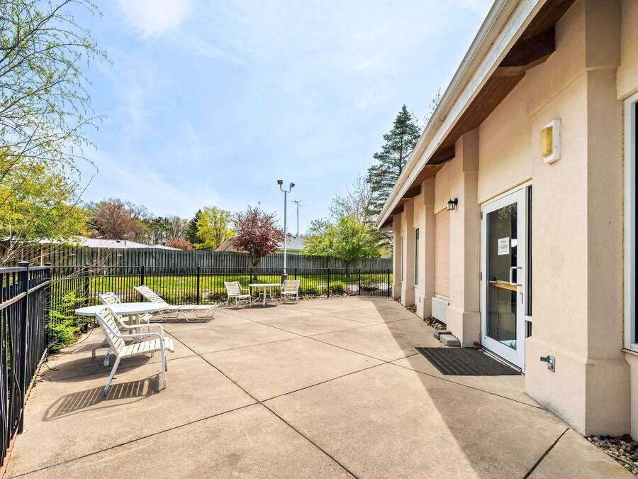 A building with a covered patio area, outdoor seating, and a fenced garden.