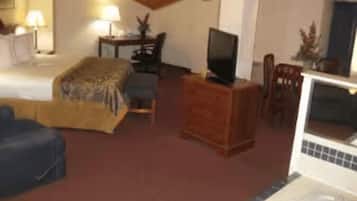A hotel room with a bed, a television on a wooden stand, a desk with a chair, and a small table with a lamp.